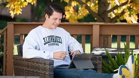 Student sitting in chair on porch studying and holding a tablet.